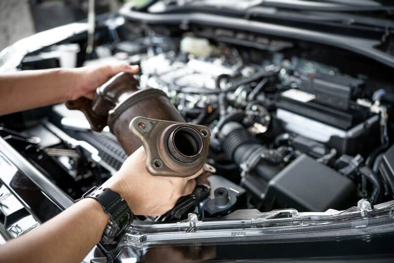 A photo of a mechanic holding a Catalytic Converter.