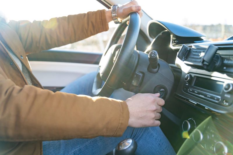 A photo of a man wearing a brown jacket, starting the engine of a car in winter.