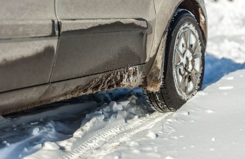 A photo of a car driving over snow in winter. There is slush build-up near the tires.
