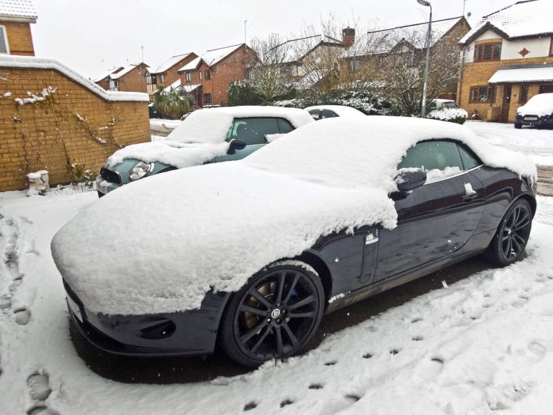 A photo of a convertible car covered in snow, parked in a driveway.