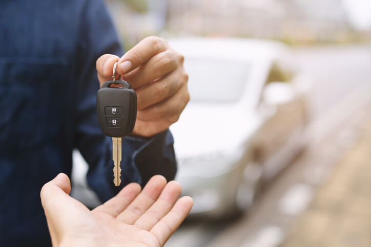 A photo of a man handing a car key to another person, with a car behind them.