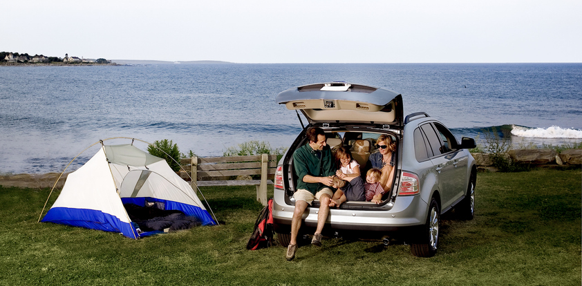 A family sitting in the back of an SUV outdoors.