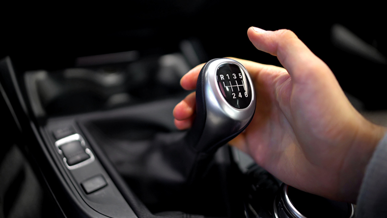 Hand holding manual gearbox in car.